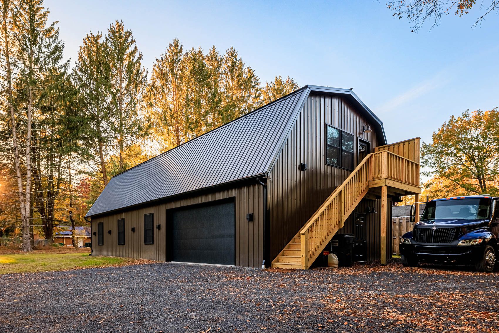 Brown gambrel-style garage with black roof, large bay door, and exterior stair access