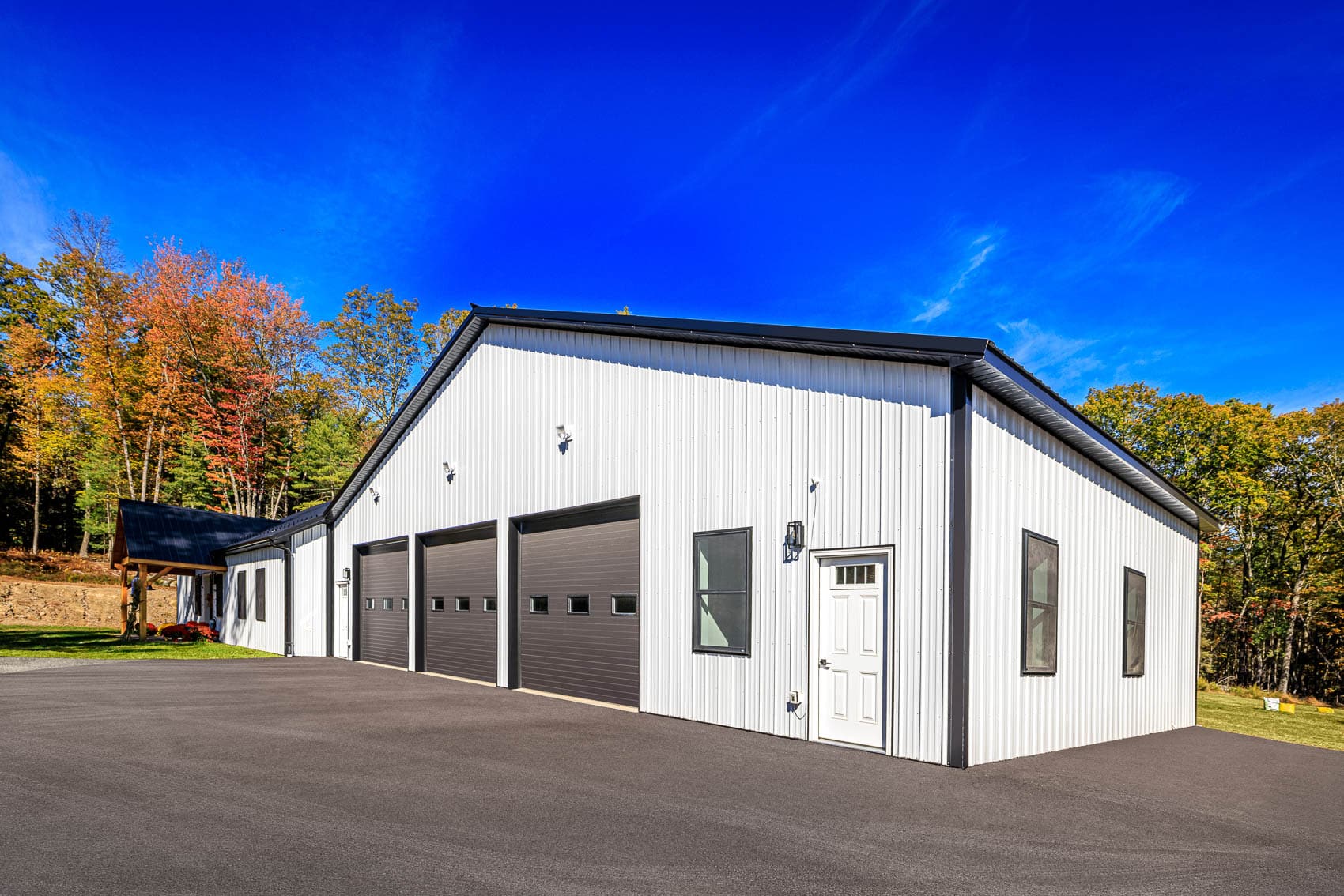 Angled view of white pole building with black garage doors and blue sky