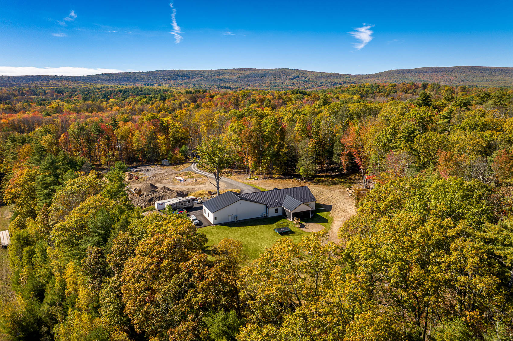 Wide aerial view of a white pole building surrounded by autumn woods