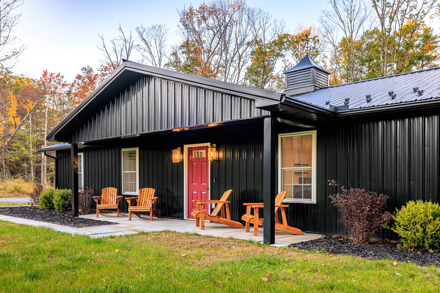 Black barndominium porch with red front door, seating, and warm lights