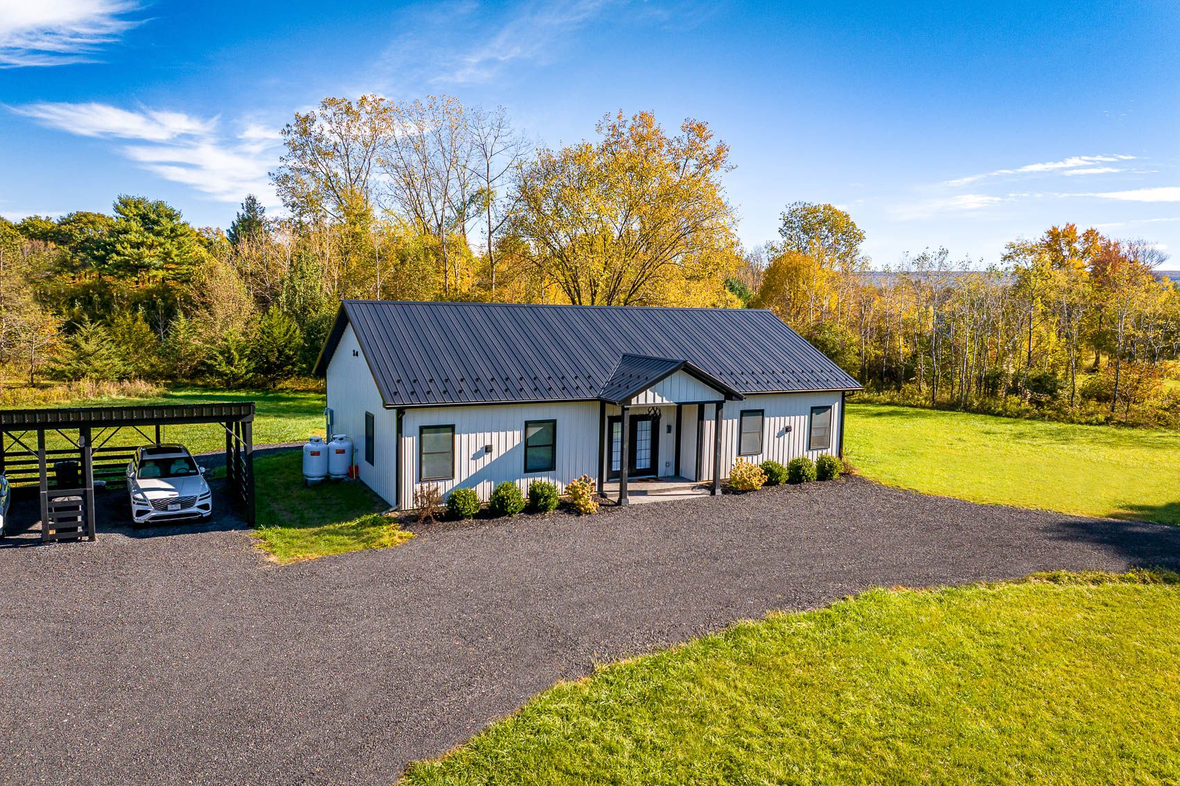 White barndominium with black metal roof, entry porch, and covered parking